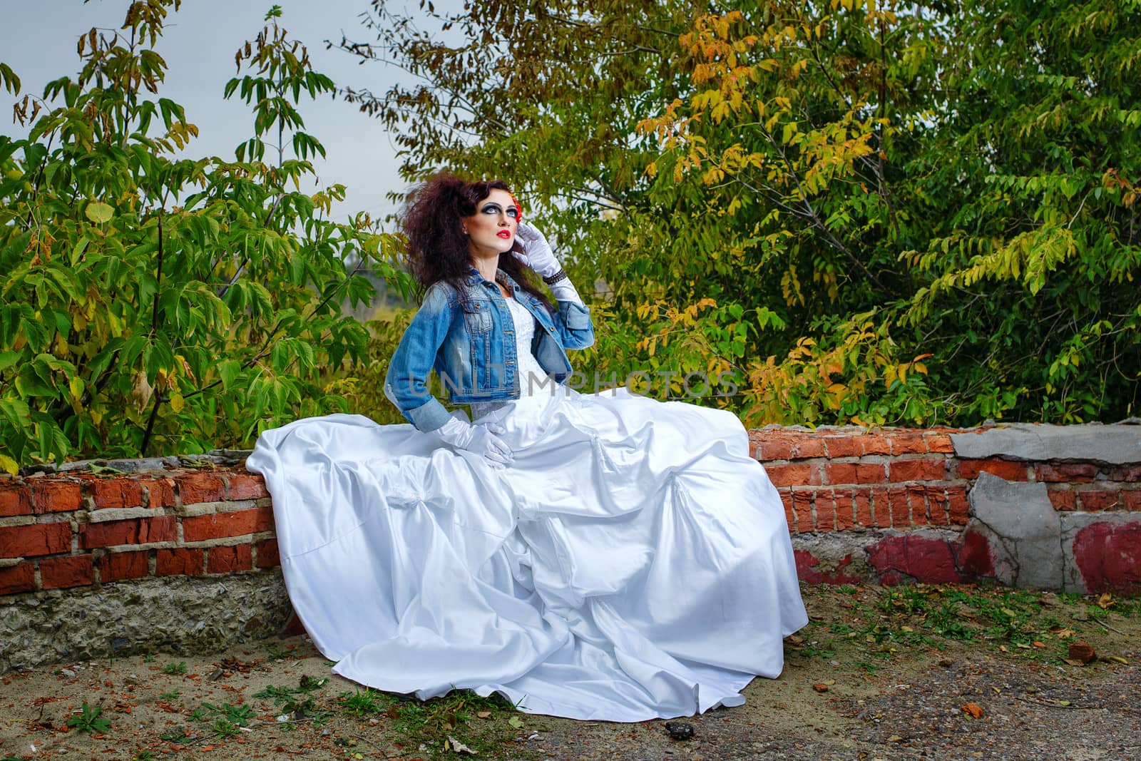 Beautiful bride in wedding dress and denim jacket in autumn park