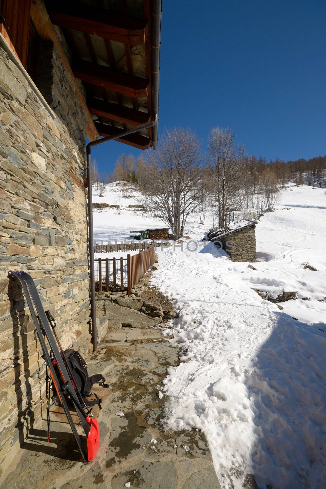 Pair of tour ski with backpack and light shovel for avalanche rescue on old stone wall of alpine hut in the italian Alps