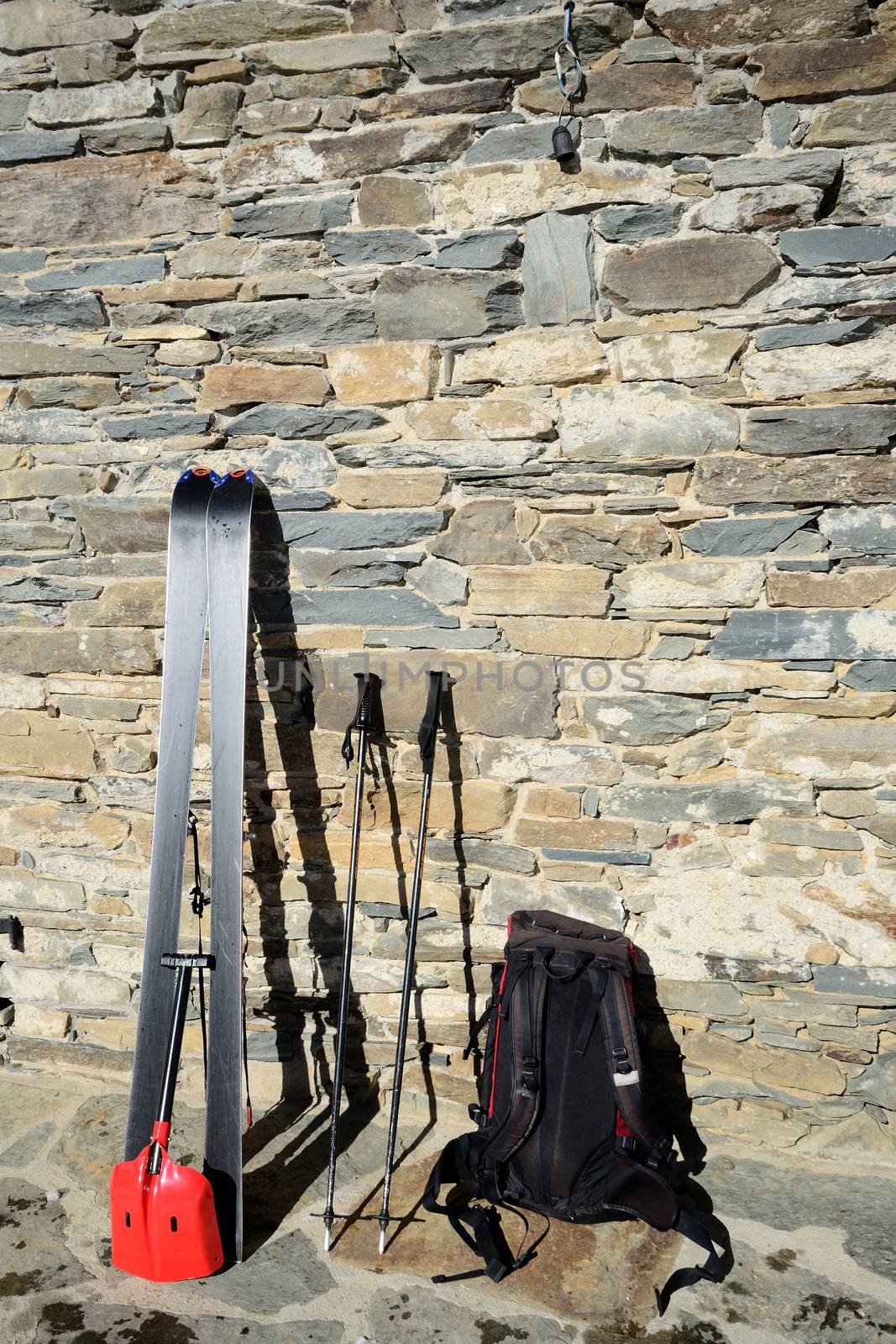 Pair of tour ski with backpack and light shovel for avalanche rescue on old stone wall of alpine hut in the italian Alps