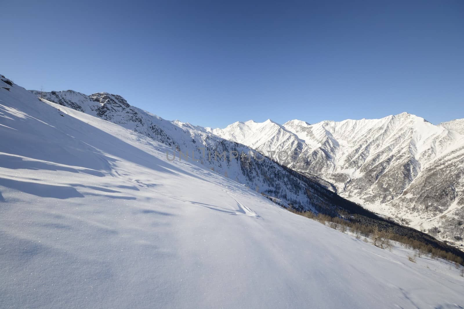 Candid off-piste ski slope in scenic background of mountain peaks, valleys and plain. Piedmont, Italian Alps