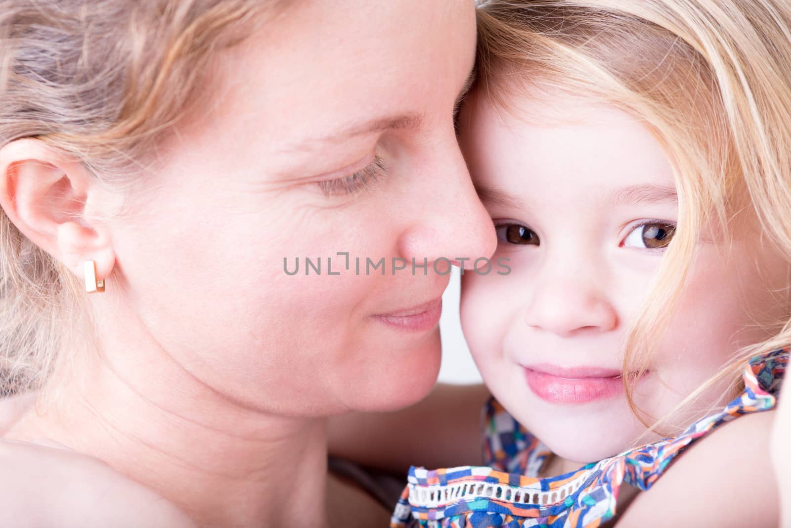 Close up of the faces of a loving devoted young mother with her pretty little daughter, both smiling with tenderness, pleasure and contentment