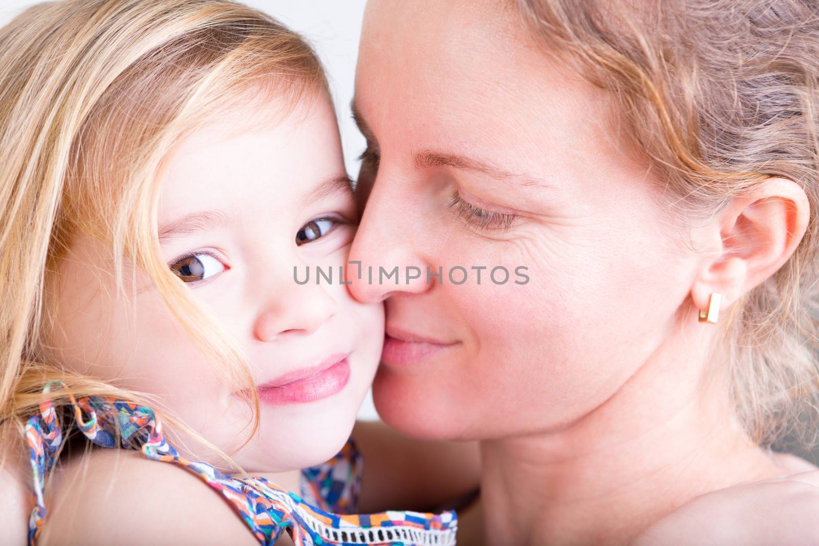 Beautiful young loving mother kissing her pretty little daughter on the cheek in a tender display of devotion