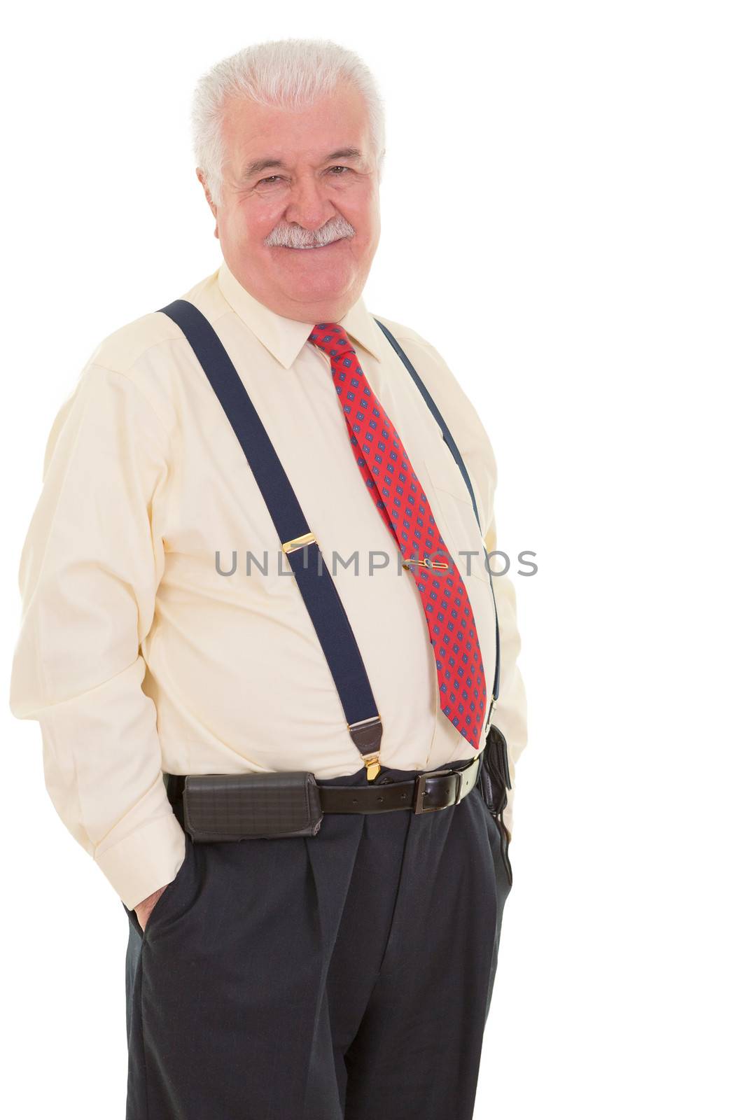 Genial senior businessman in braces standing in a confident relaxed pose with his hands in his pocket smiling at the camera, three quarter isolated on white
