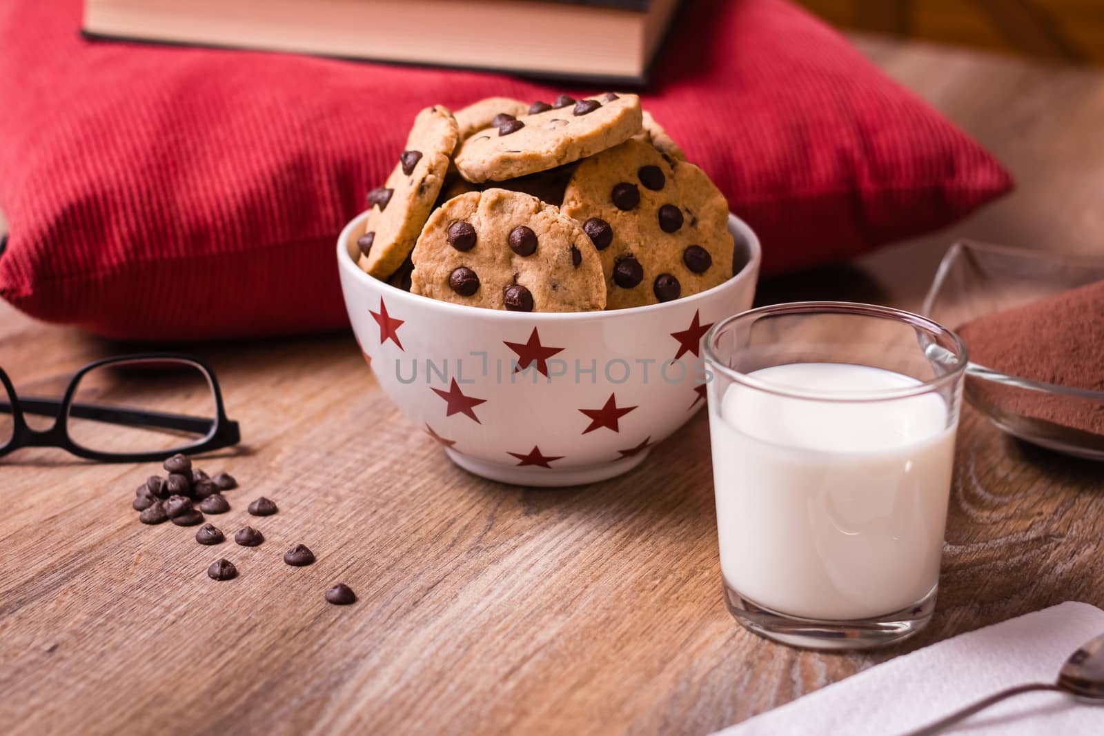 Closeup of chocolate chip cookies on stars bowl and milk glass over a wooden background