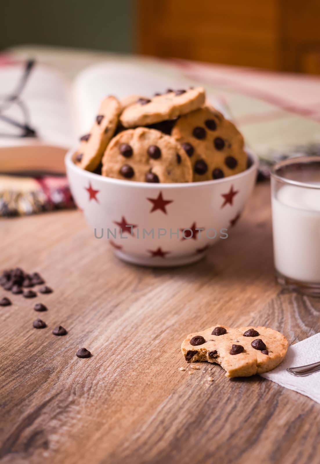 Closeup of chocolate chip cookies on stars bowl and milk glass over a wooden background. Image focused in cookie bite