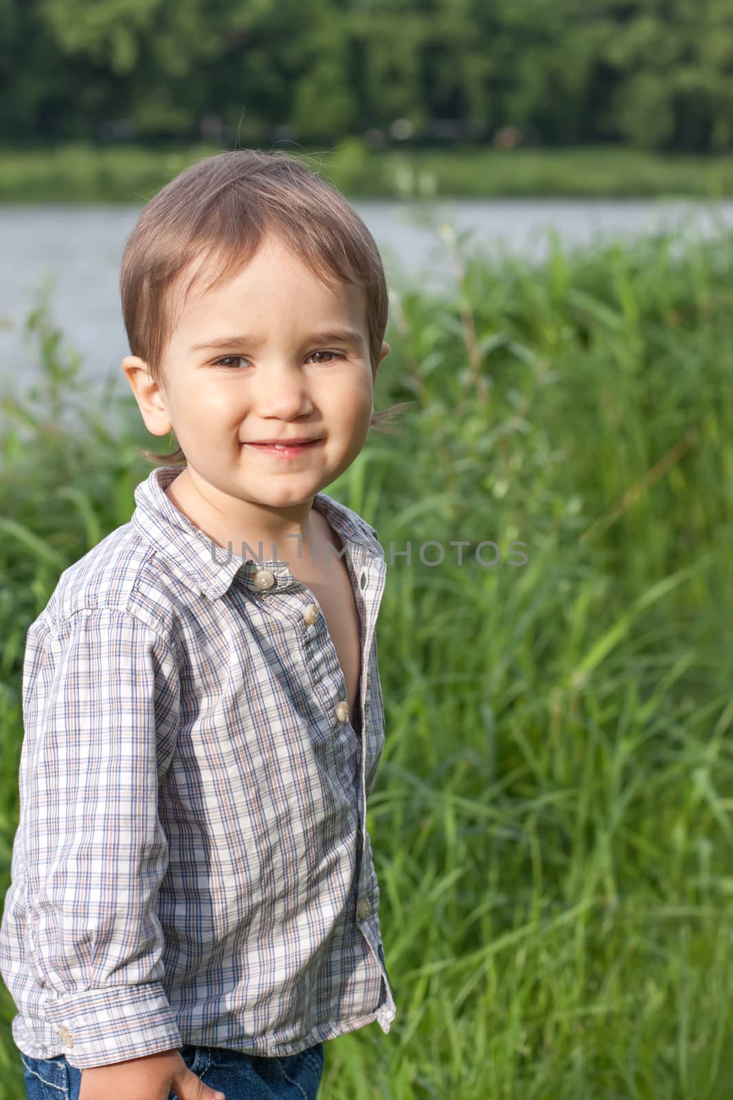 Little boy play in green grass near the river