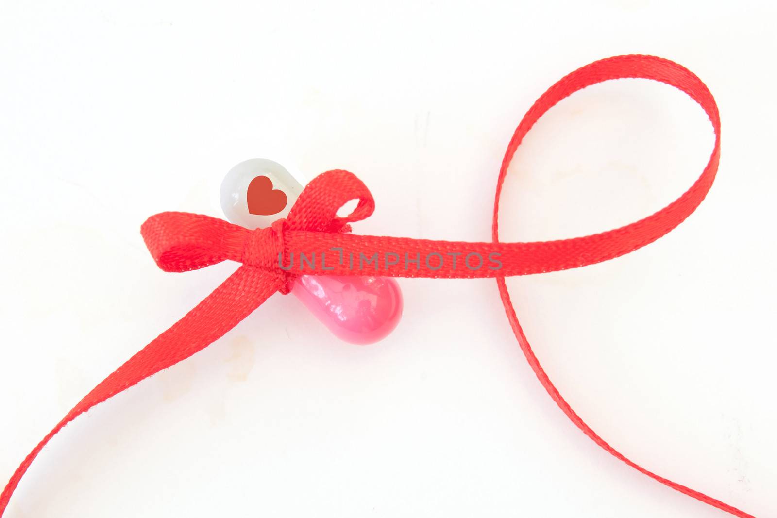 Red ribbon tied around a capsule with a heart symbol 