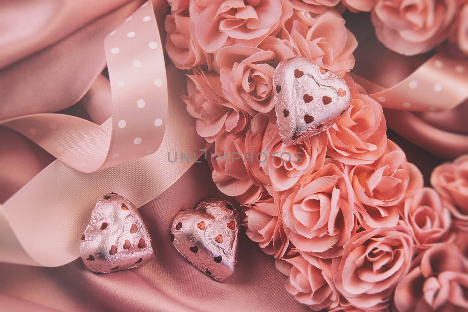 Heart made of pink roses with ribbons and chocolates on satin