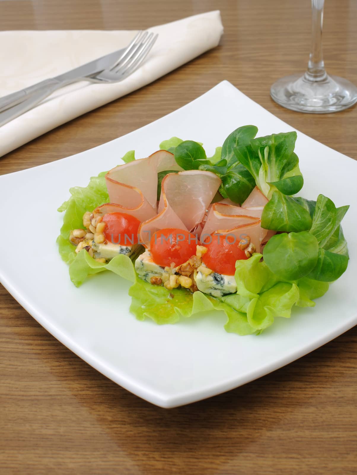 Jamon with blue cheese under the walnut sauce and cherry tomatoes in salad leaves