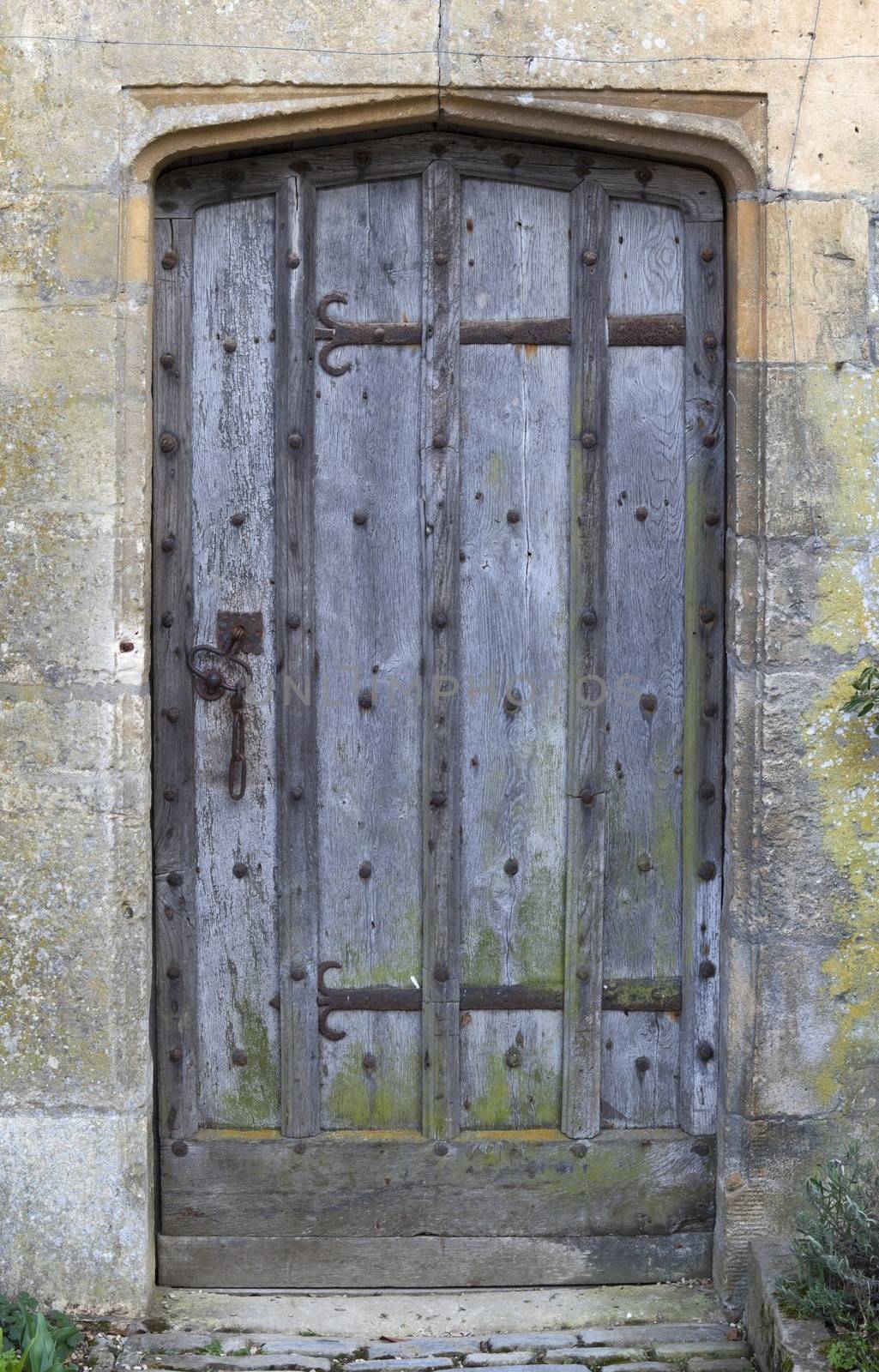 Old studded oak door set into Cotswold stone wall, Gloucestershire, England.