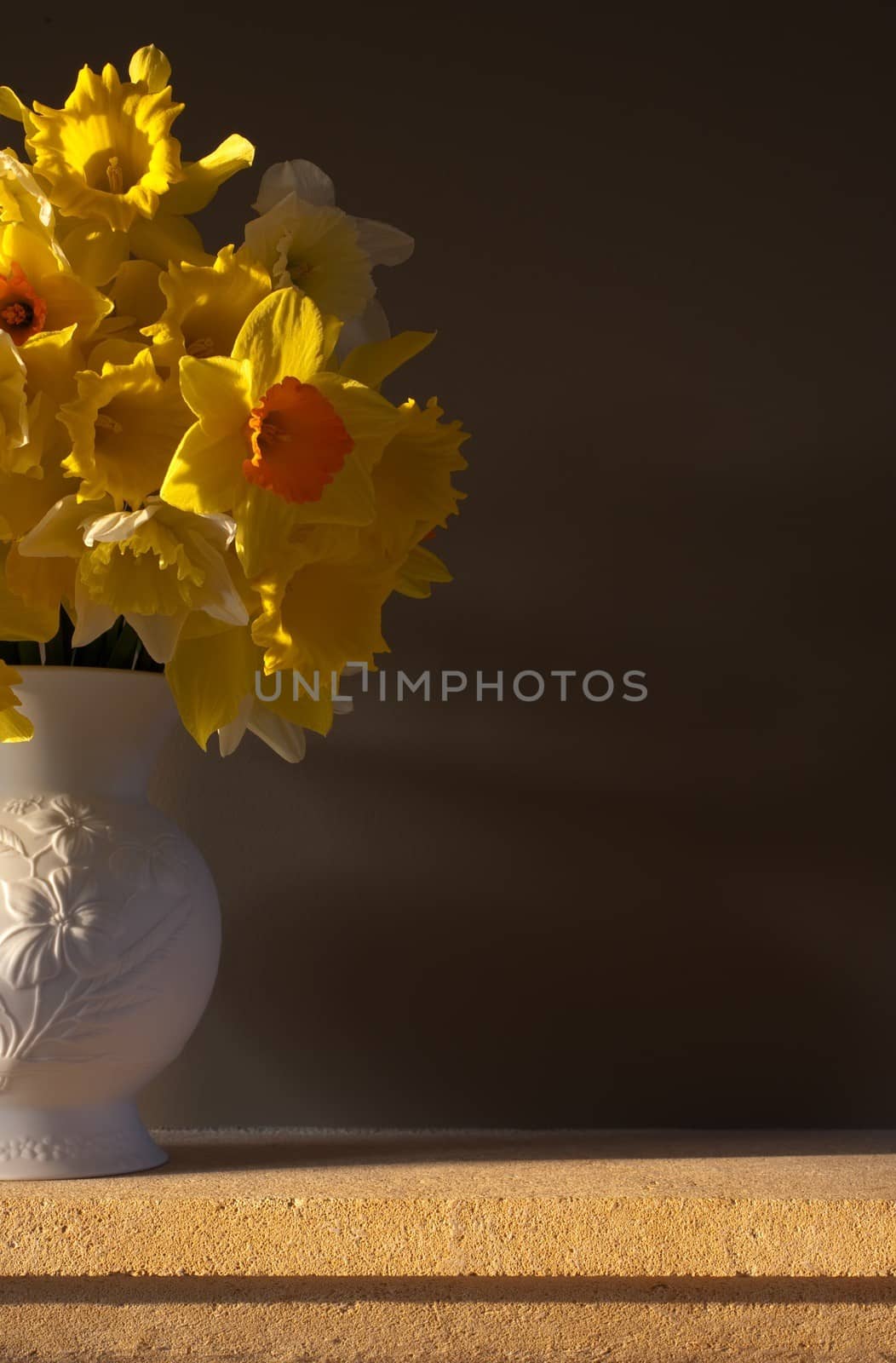 Daffodils in a white vase on a Cotswold stone mantlepiece against a plain background.