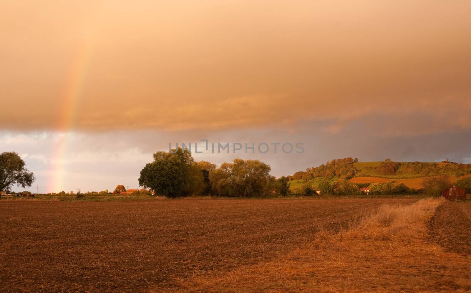 Looking towards Meon Hill over farmland with a dramatic sunset and rainbow, Gloucestershire, England.