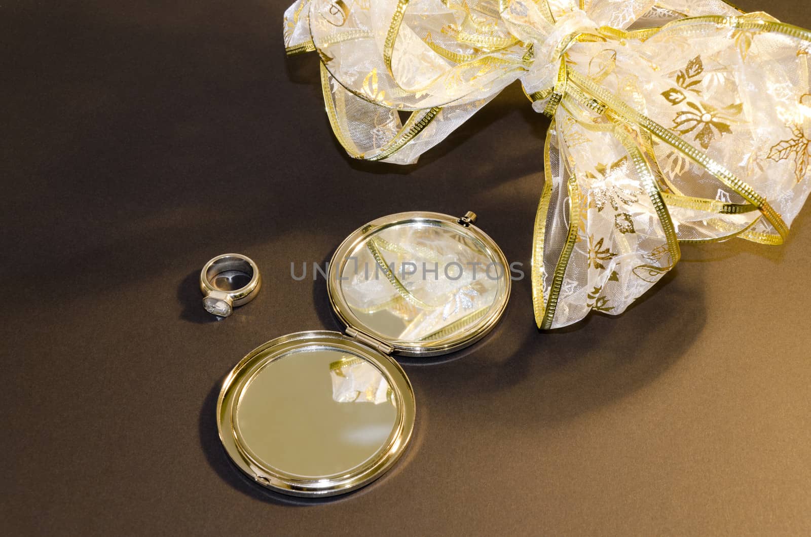 Composition with a mirror, a ring and a bow on a brown background