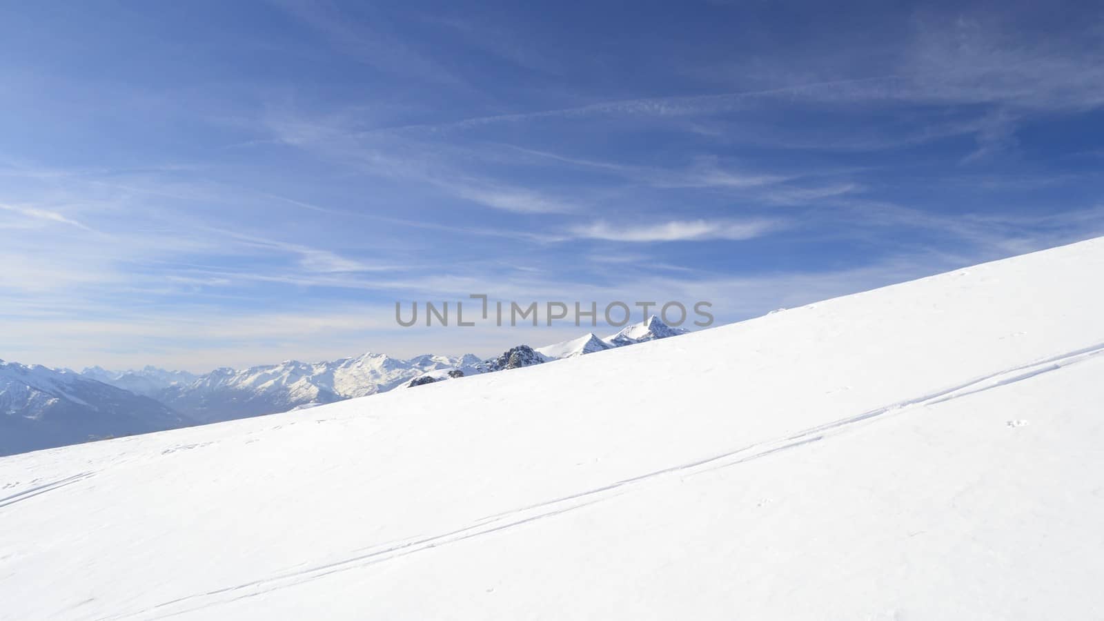 Candid off-piste ski slope in scenic background of mountain peaks, valleys and plain. Piedmont, Italian Alps
