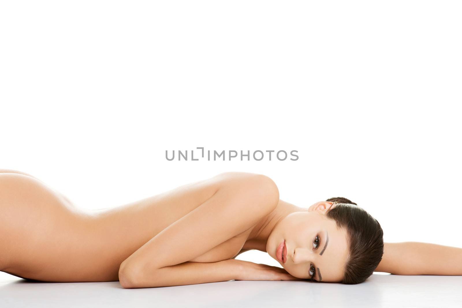 Beautiful happy naked woman with fresh clean skin lying on belly