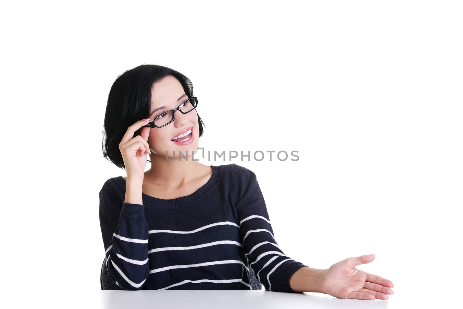 Young woman sitting at the desk and showing something, isolated on white background