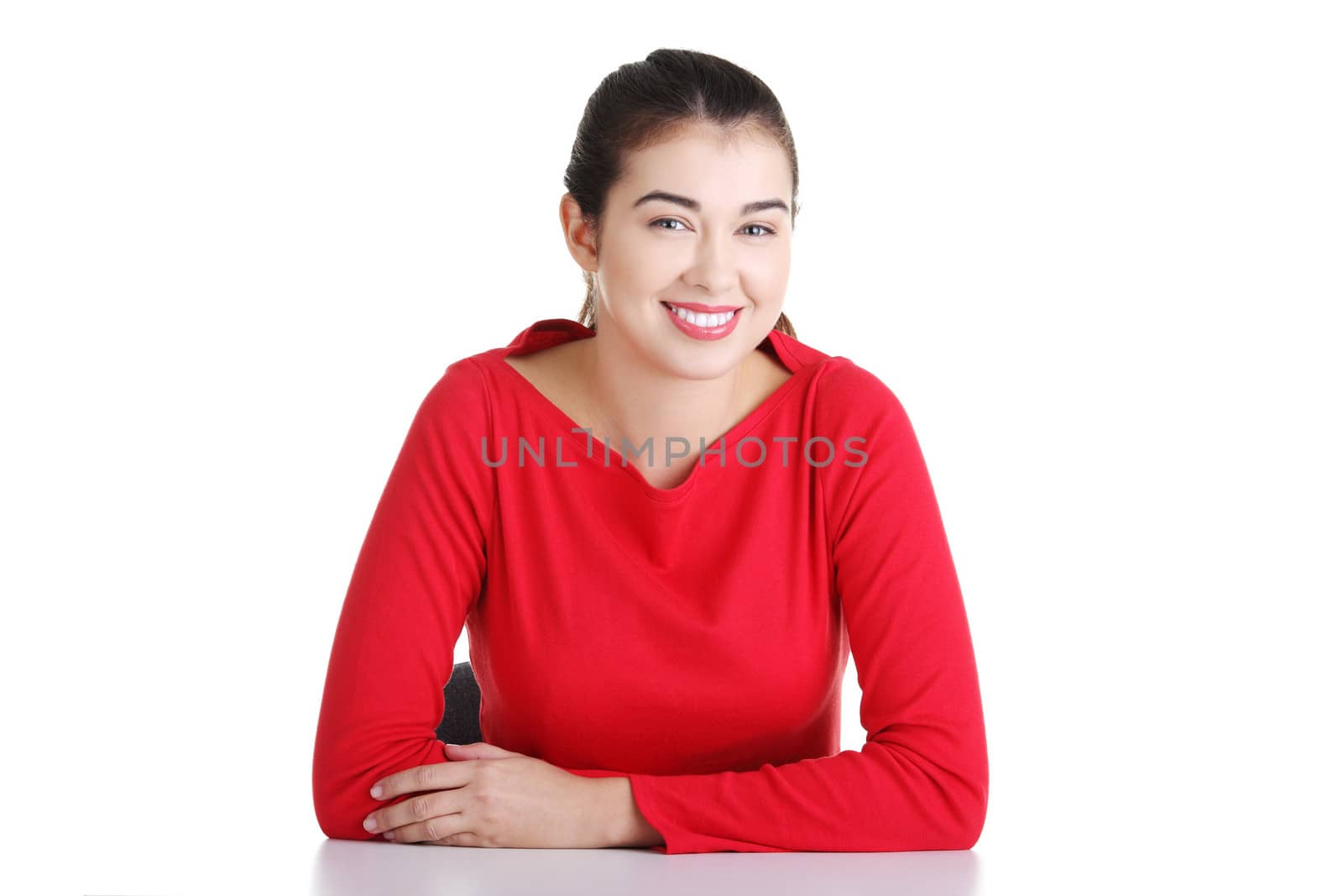 Pretty, happy, young woman in casual clothes sitting at the desk, isolated on white