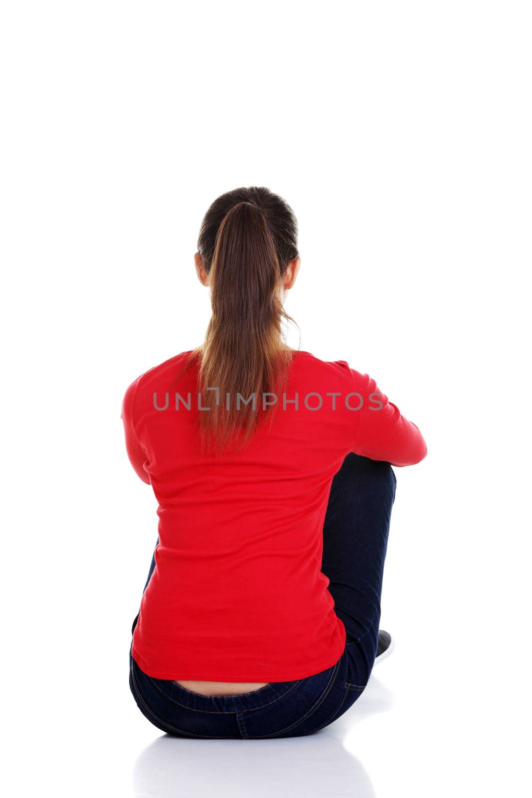 Back view of beautiful young woman sitting on the floor and looks into the distance. Isolated over white background.