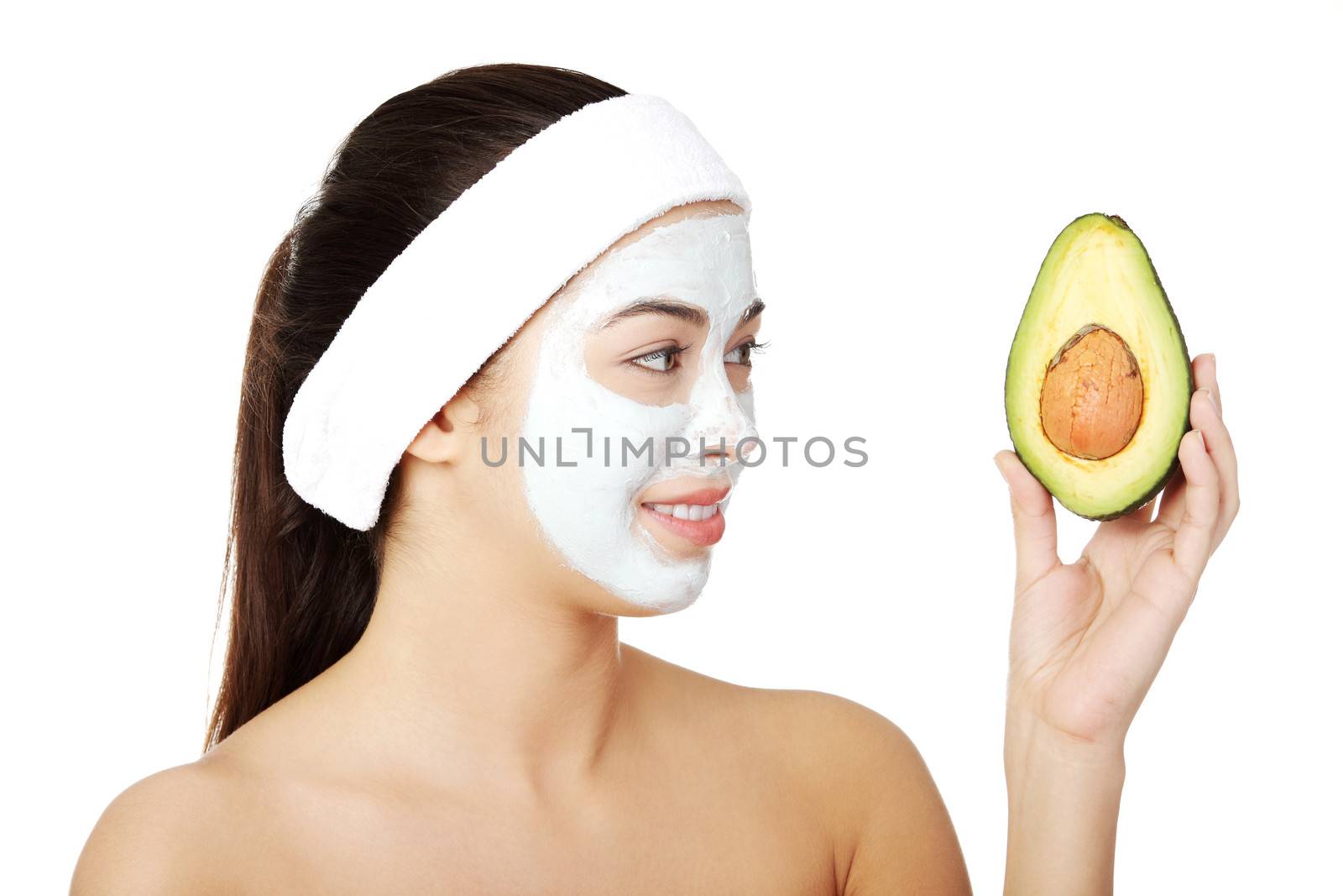 Young woman holding avocado heaving face clay mask on the face in a spa