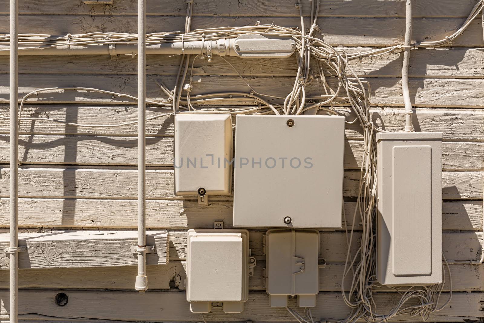 Messy cables and electrical boxes in a wooden beige painted wall facade