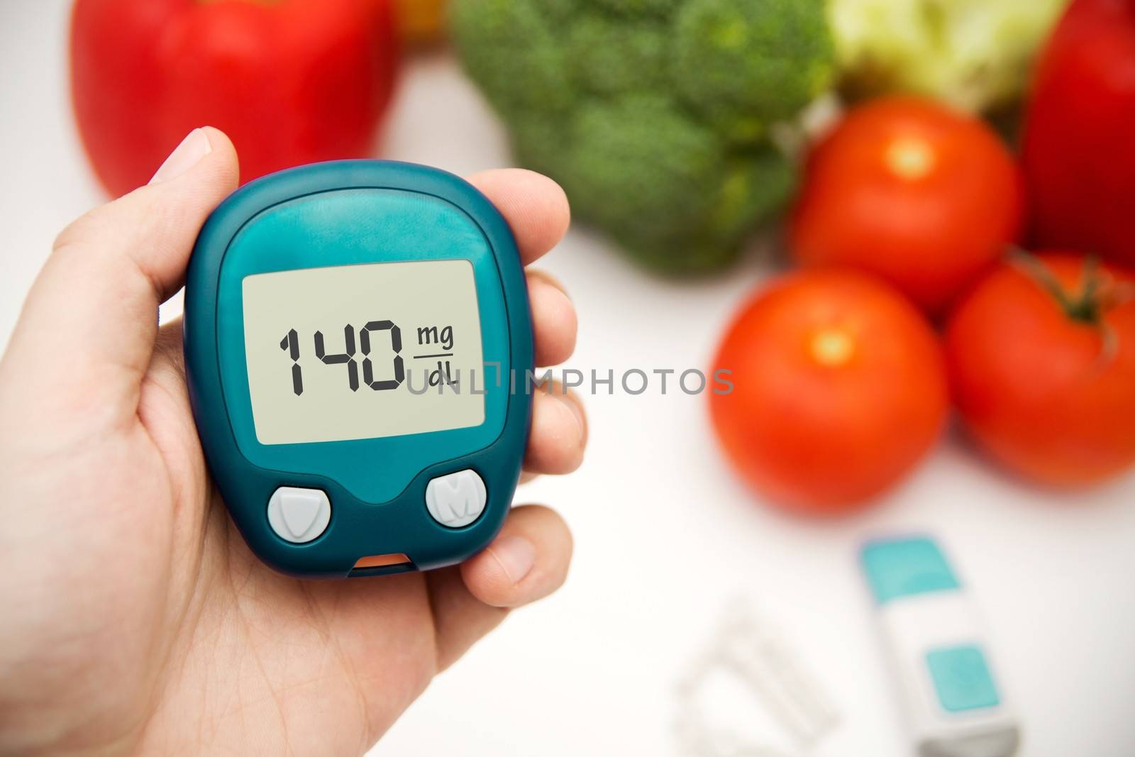 Hand holding meter. Diabetes doing glucose level test. Vegetables in background