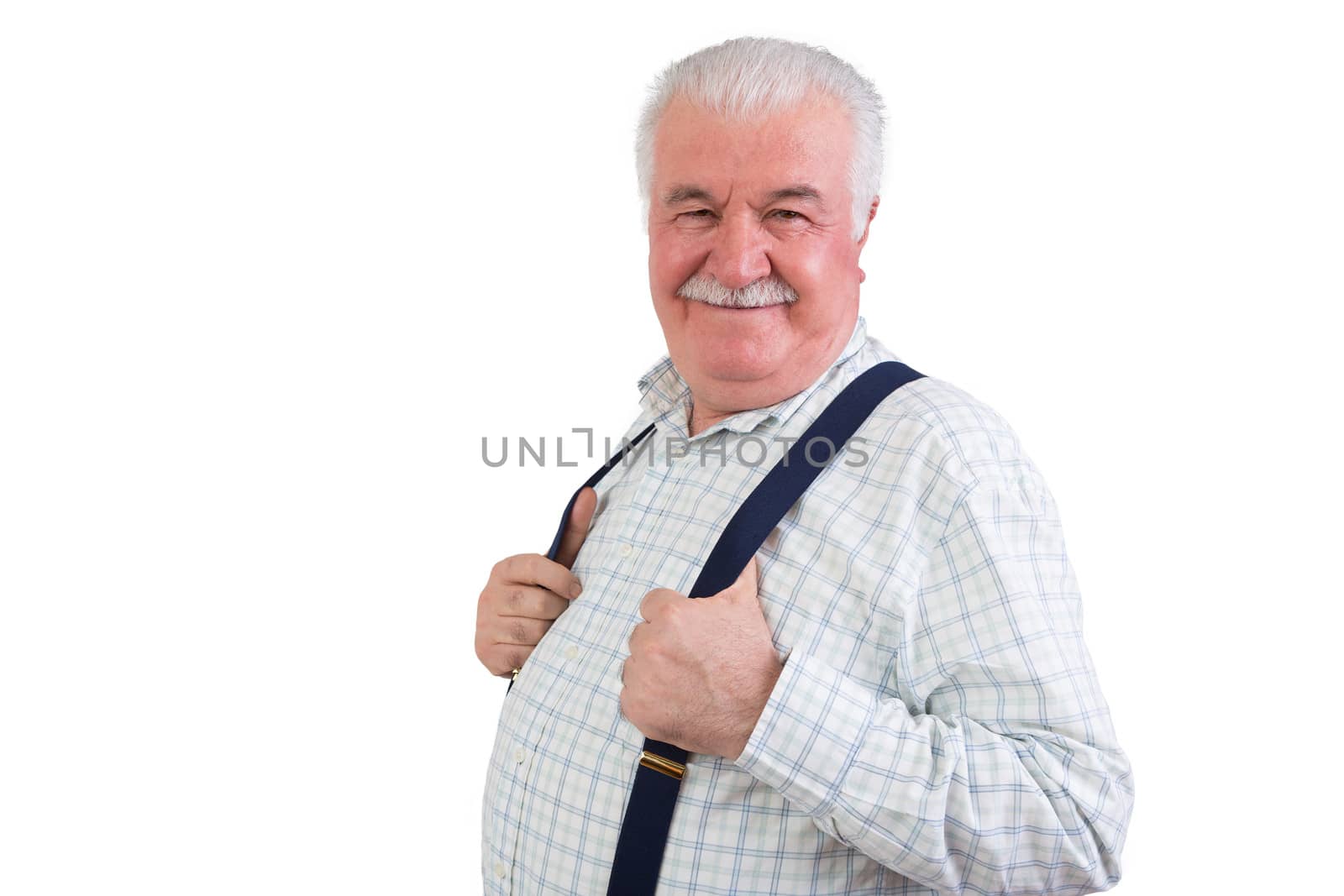 Jovial confident elderly man with a moustache and his hands hooked through his suspenders beaming happily at the camera, upper body isolated on white