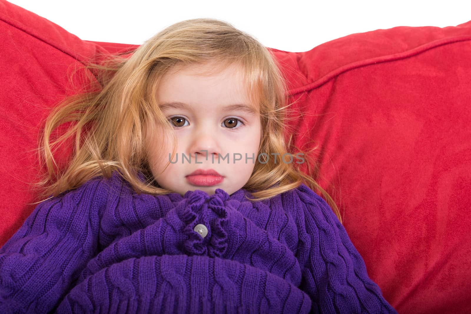 Cute solemn beautiful young girl staring at the camera with a calm expression as she relaxes on a comfortable red cushion in her colourful purple sweater
