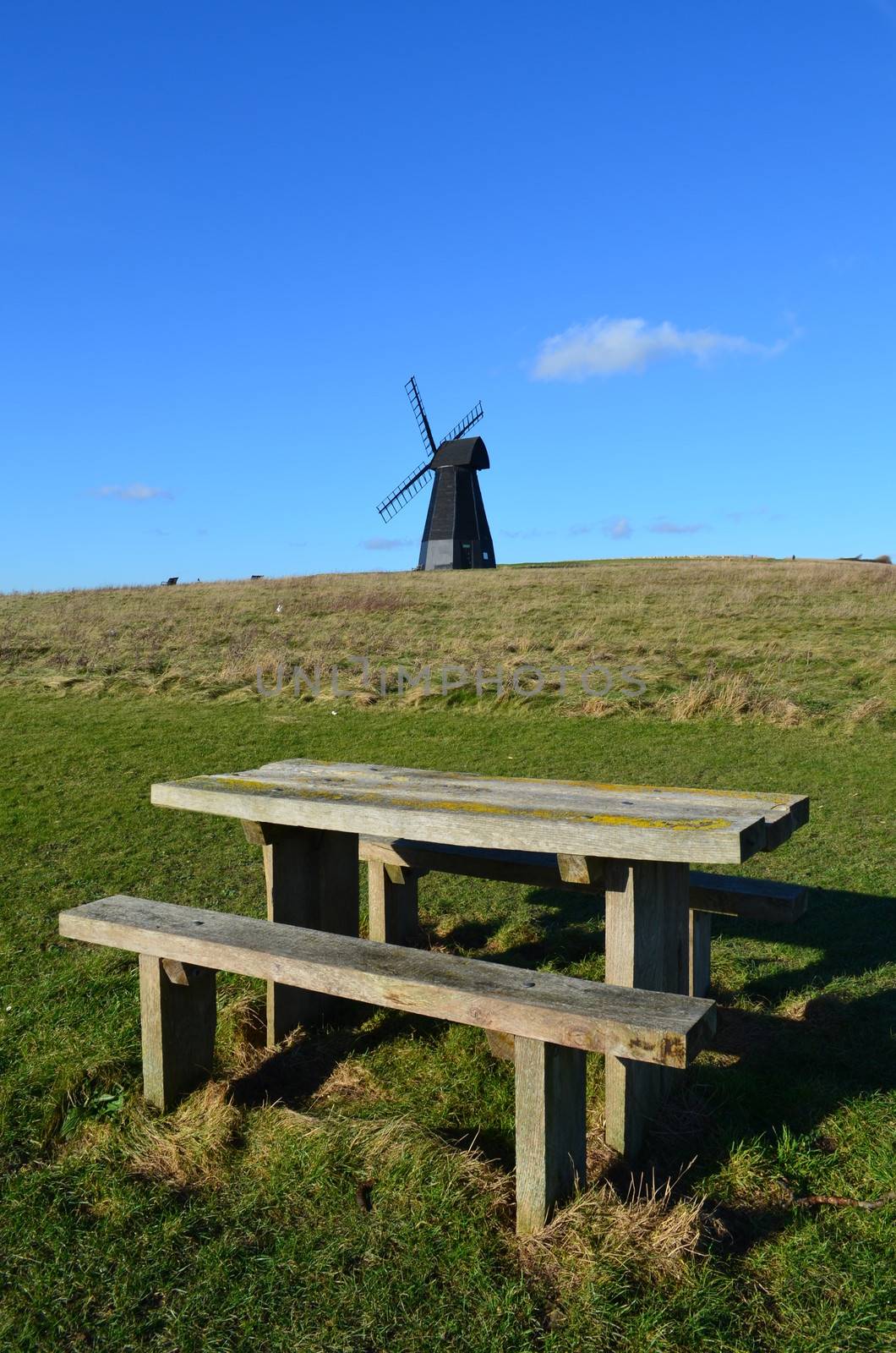 Wood picnic table and bench with a traditional Sussex Smock windmill in the background.Image taken at Rottingdean,Brighton,England.