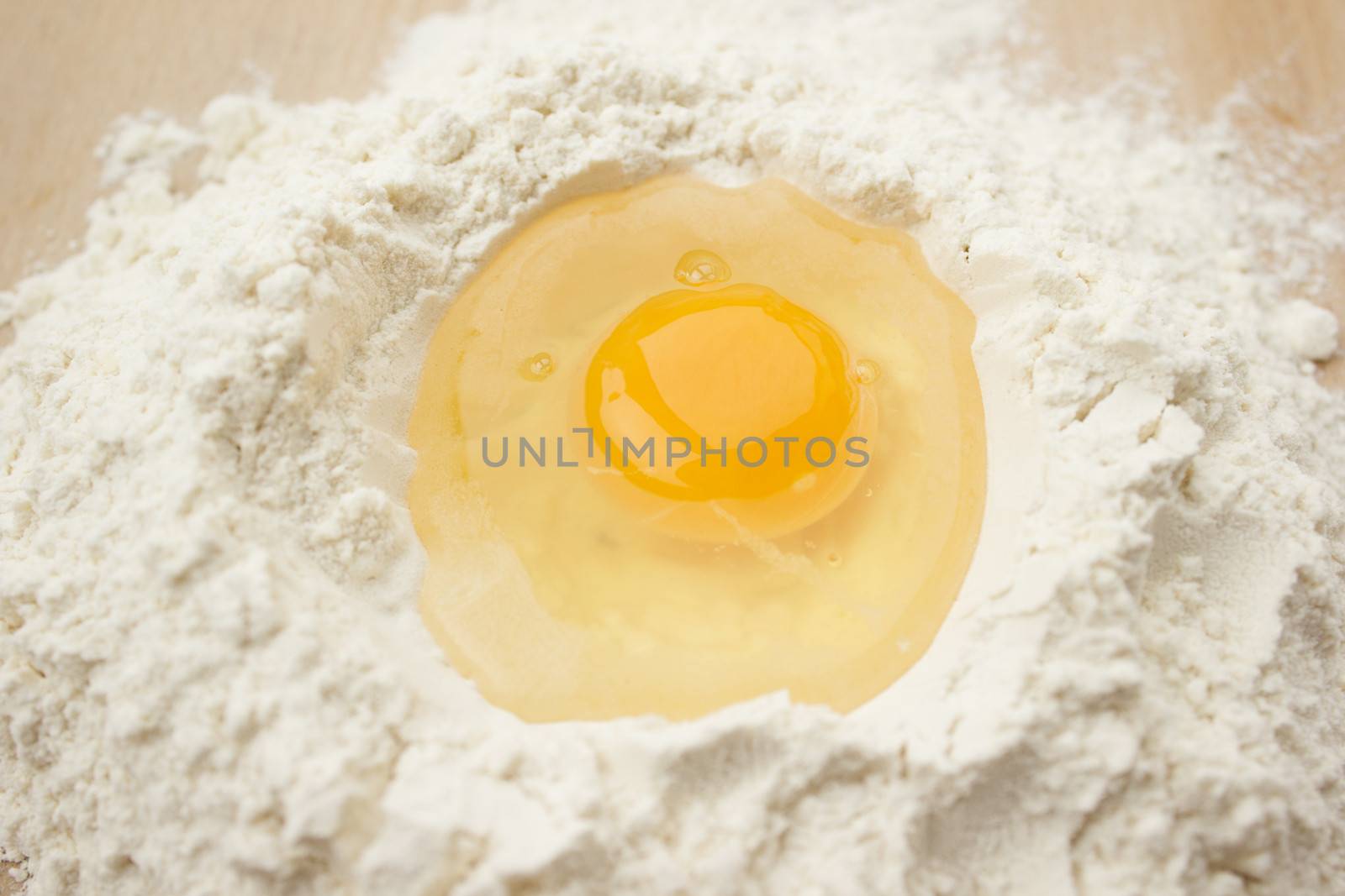 Flour on a wooden cutting board with a egg in the middle of it.