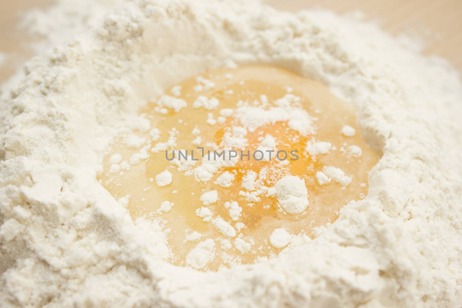 Flour on a wooden cutting board with a egg in the middle of it.