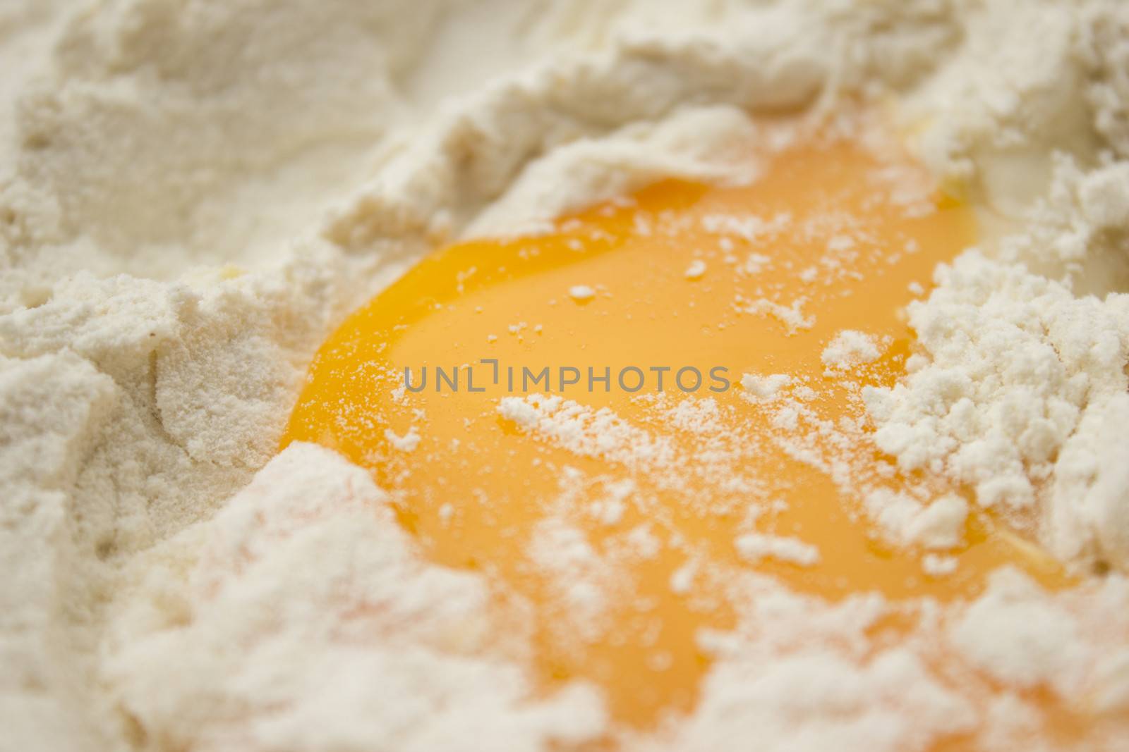 Flour on a wooden cutting board with a egg in the middle of it.