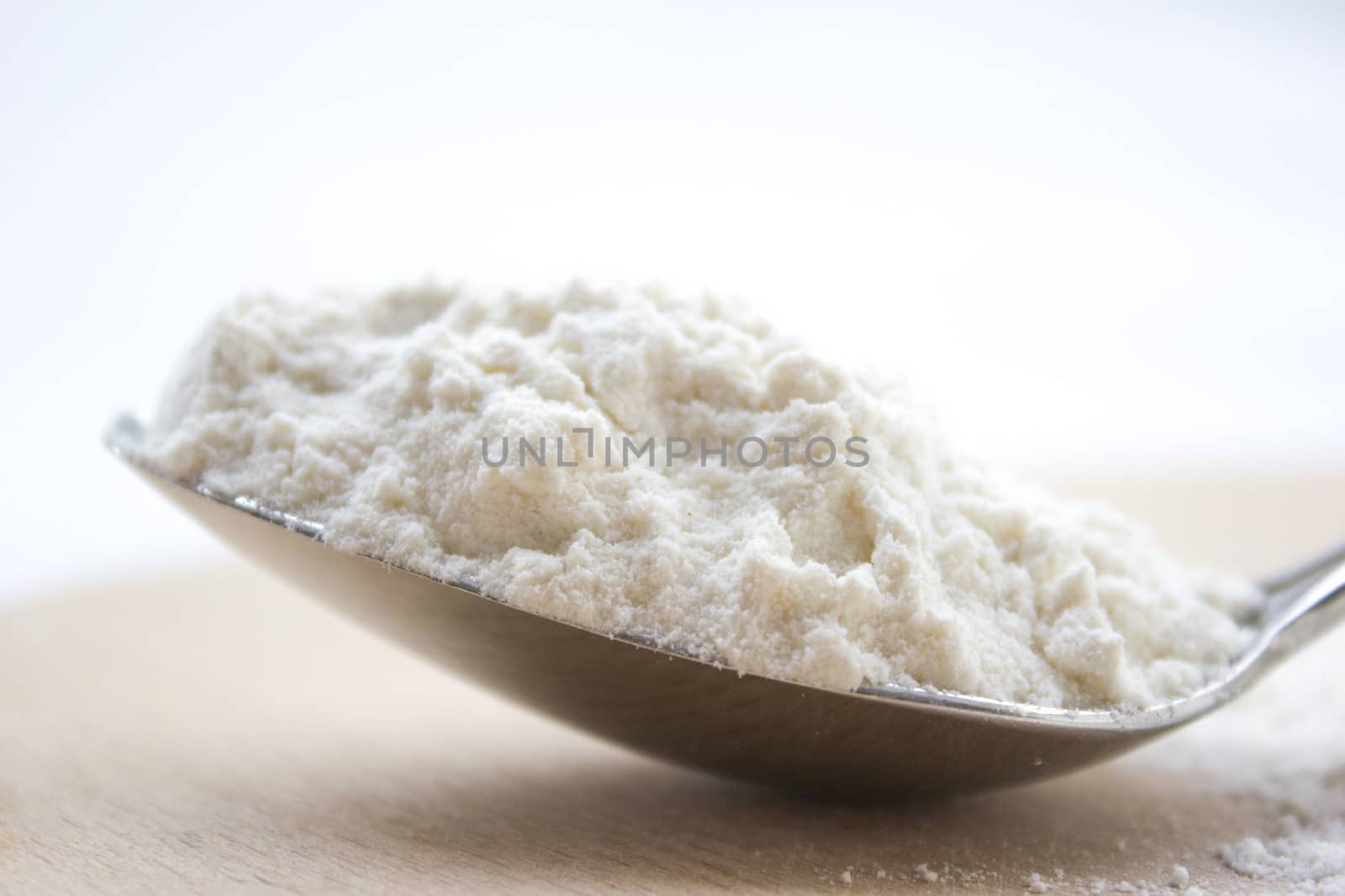 Metal spoon full with flour on a wooden cutting board.