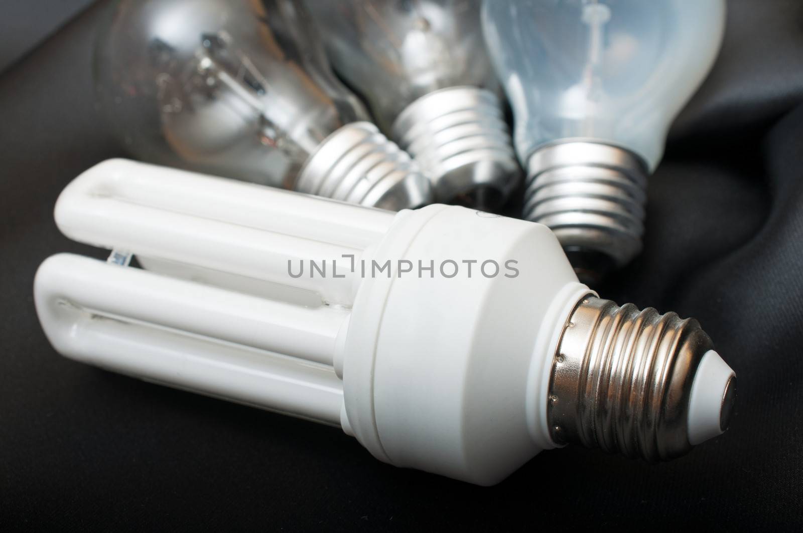 Energy Saving Bulb and Three Aged Burnt Tungsten Bulbs on Black Background