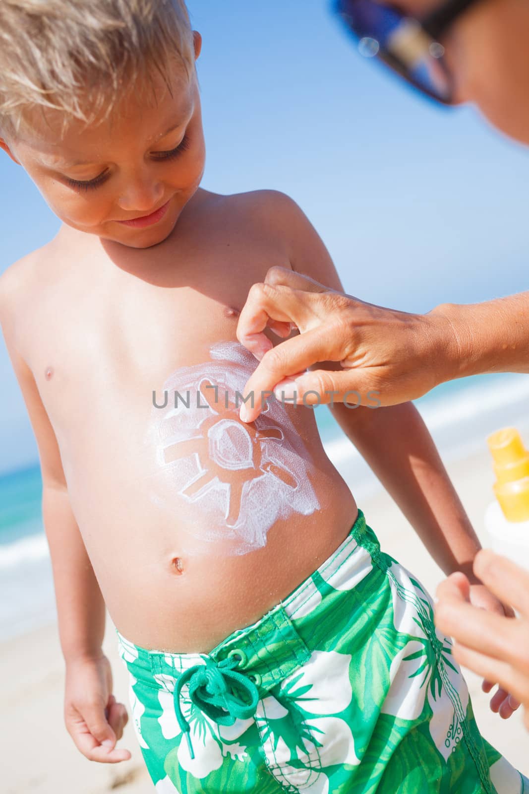Adorable boy and mother at tropical beach applying sunblock cream.