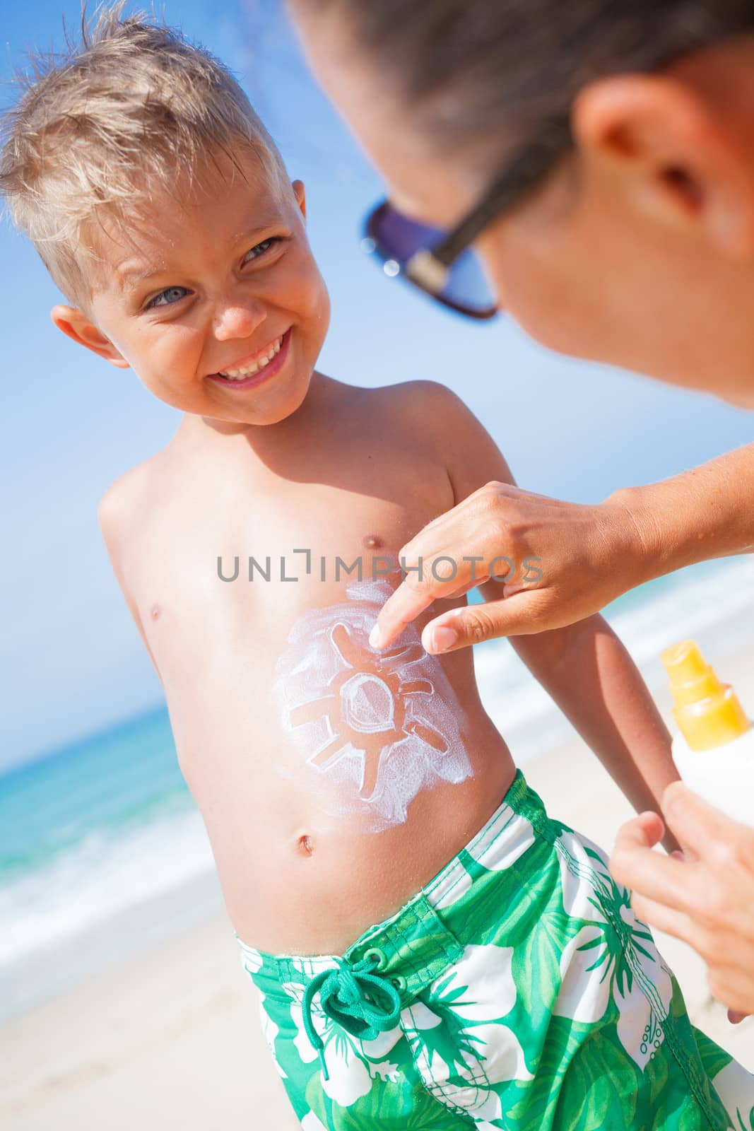 Adorable boy and mother at tropical beach applying sunblock cream.
