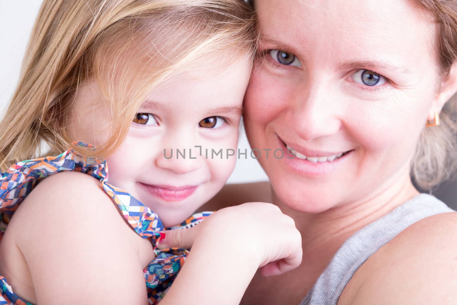Close up facial portrait of a happy smiling beautiful little girl with her mother looking at the camera sharing a tender moment