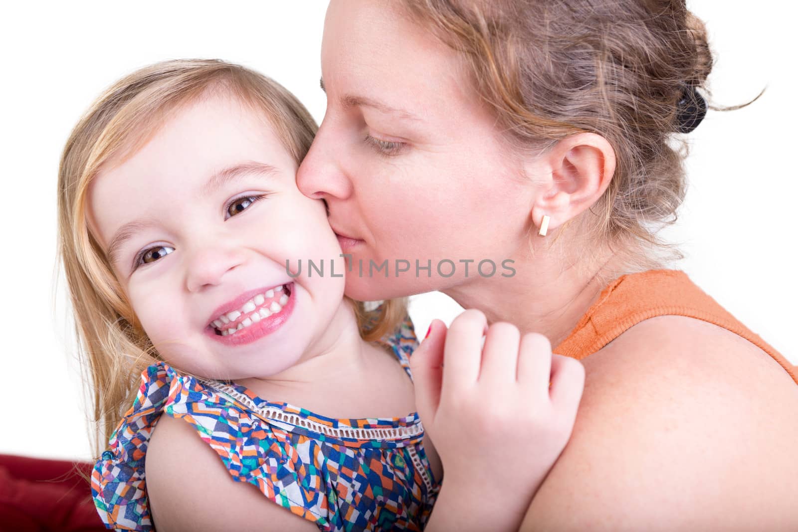 Adorable pretty little blond girl laughing as she is kissed on the cheek by her beautiful young mother