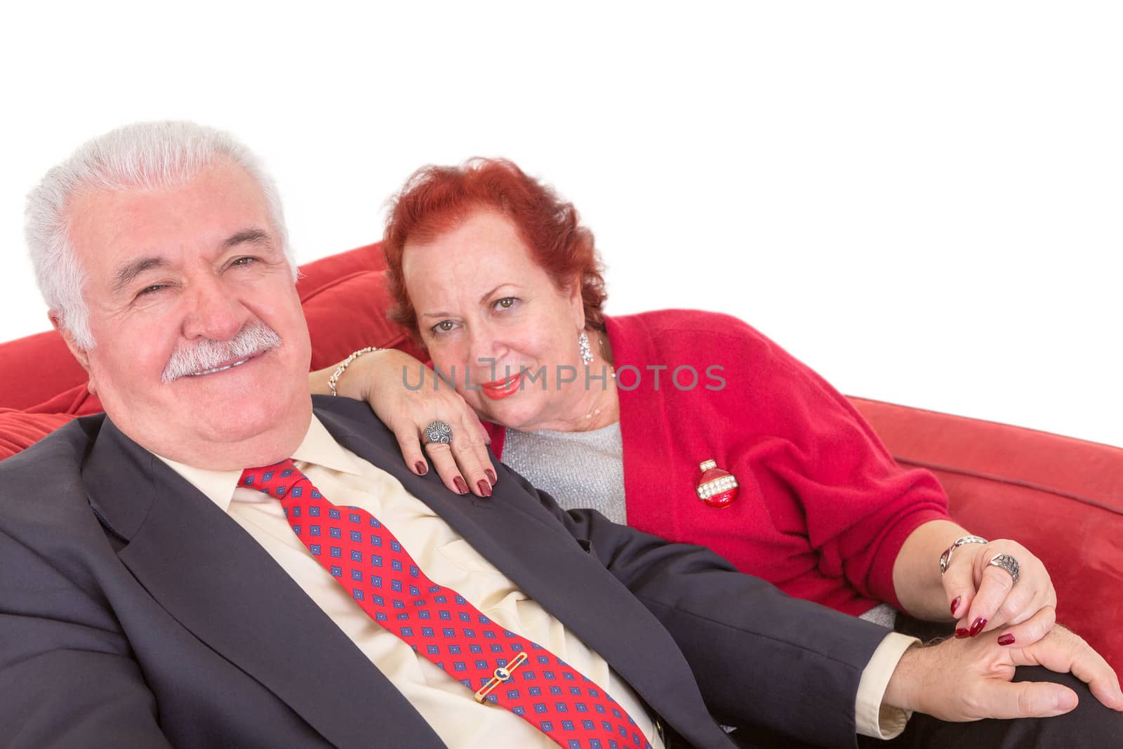 Stylish elderly couple sitting on a red sofa by coskun