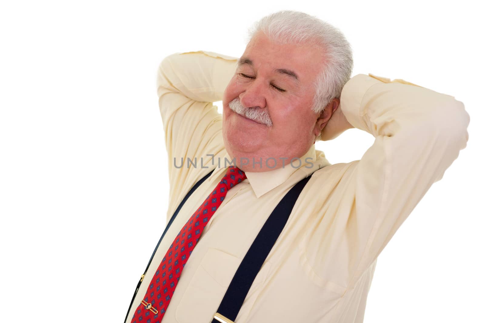 Contented grey-haired senior man with a moustache wearing suspenders relaxing with his hands behind his head and his eyes closed with a smile of satisfaction, on white