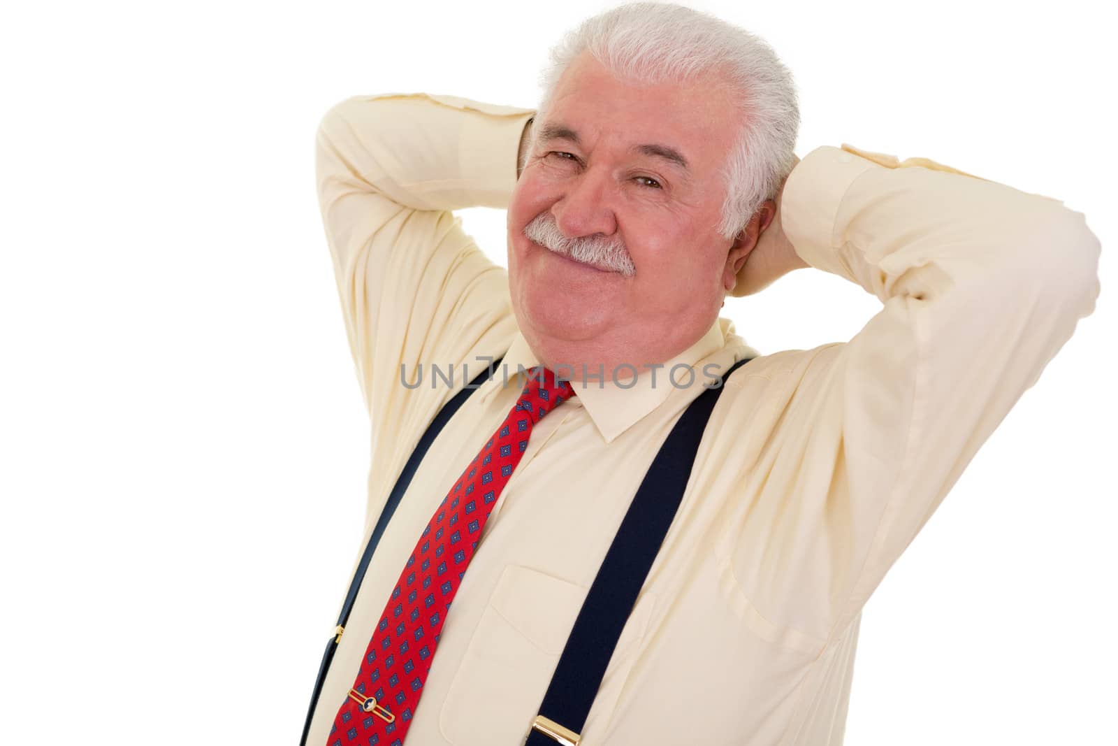 Smiling senior businessman relaxing with his hands behind his head in a red tie and braces, isolated on white