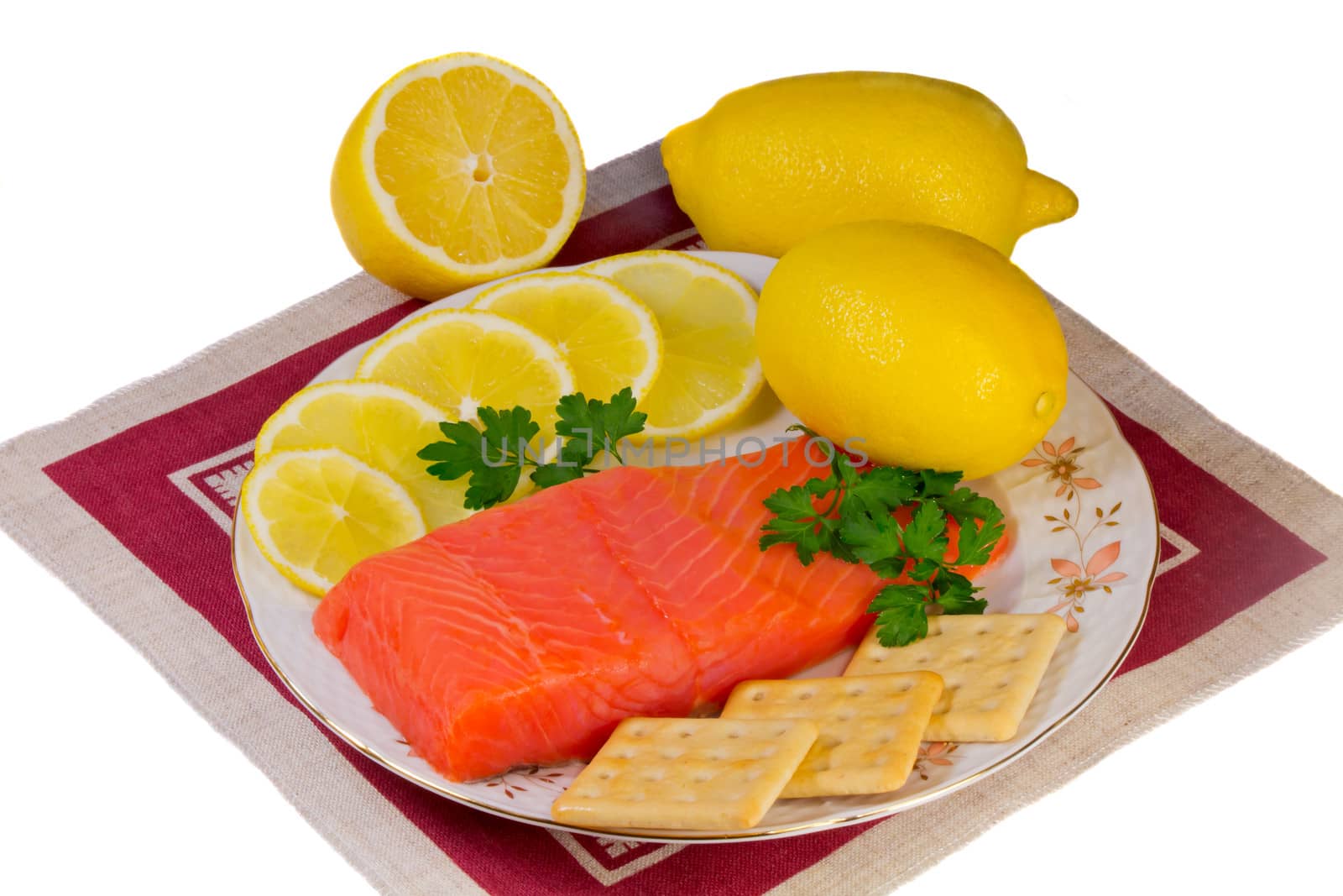 On a platter lie salmon fillet, lemons, sliced and whole, biscuits, fresh herbs parsley. Presented on a white background.