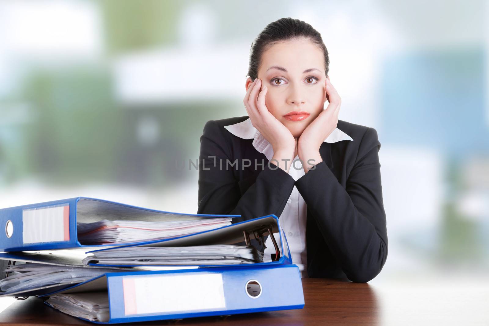 Sad woman with ringbinders sitting at the desk. Tired and exhousted business woman.