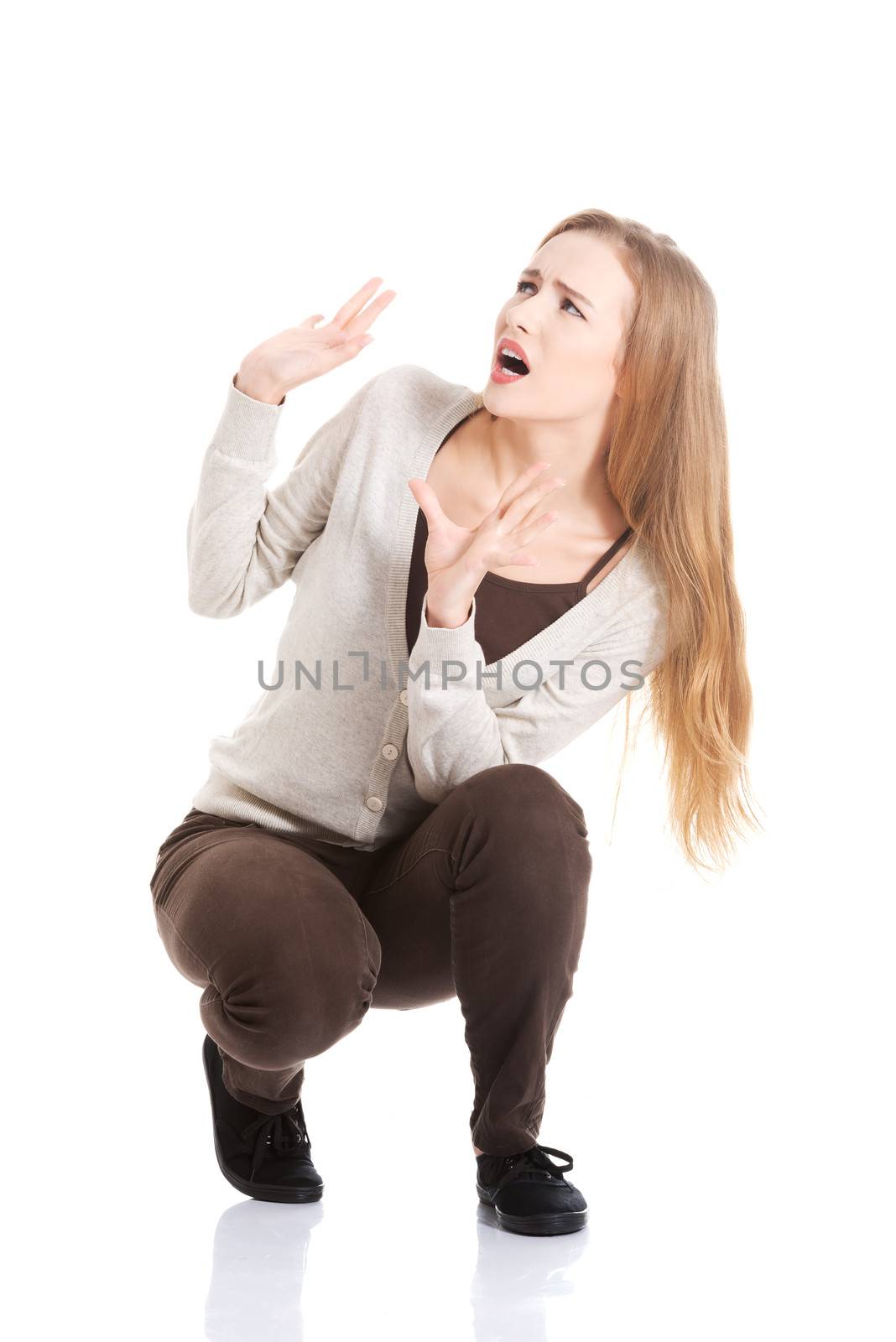 Beautiful casual woman is crouching from sth heavy above her. Isolated on white.