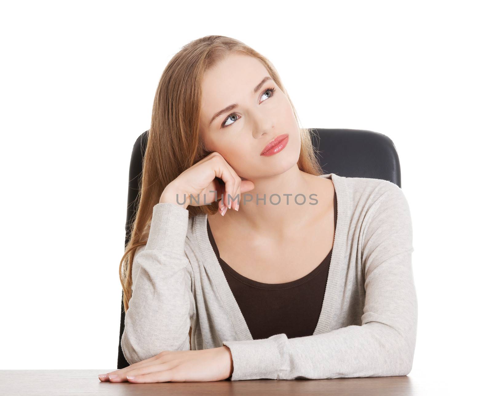 Beautiful casual woman sitting by a desk and day- dreaming. Isolated on white.