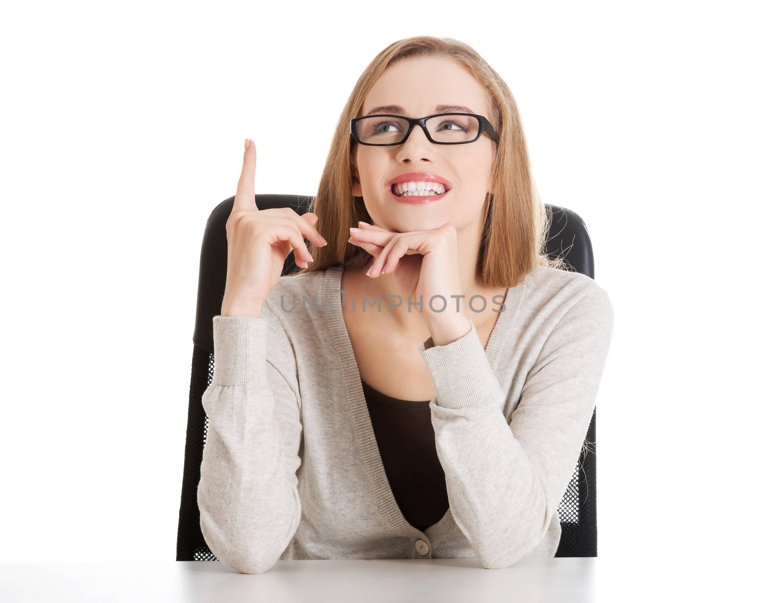 Beautiful casual woman sitting and pointing up, advertising. Isolated on white.