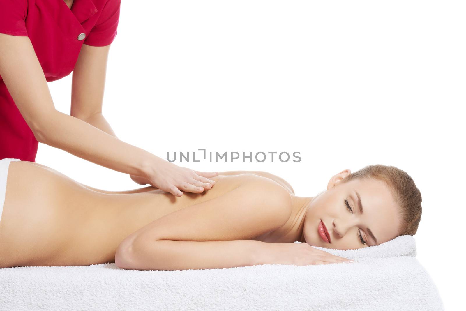 Young beautiful caucasian woman lying on a massage table and is being massaged. Isolated on white.