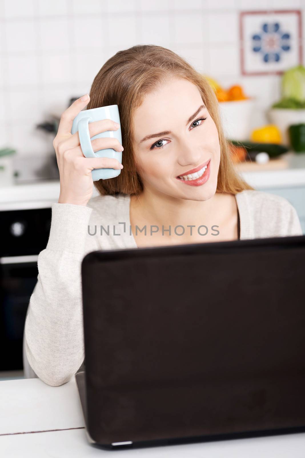 Young beautiful woman sitting by the table with laptop and cup. by BDS