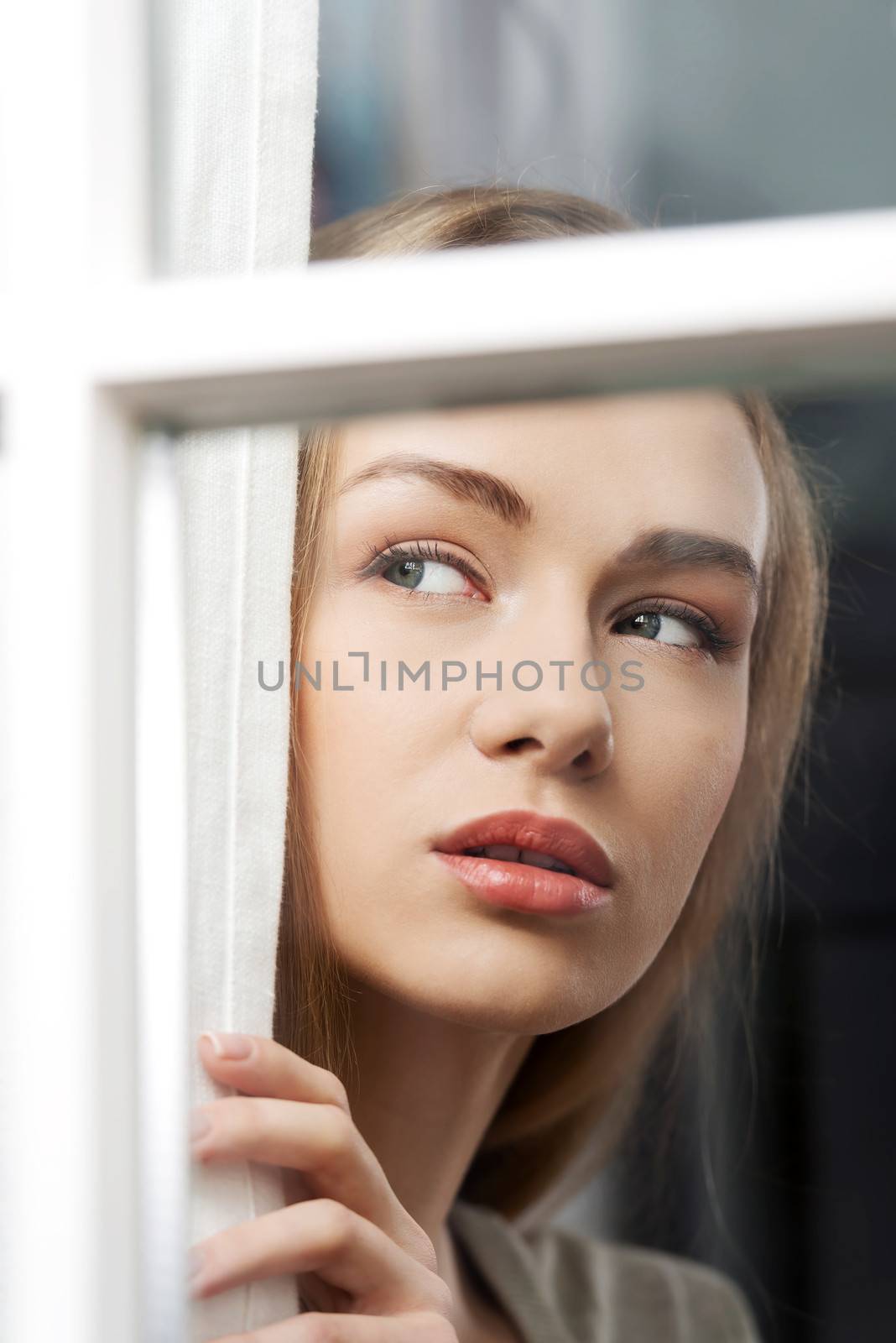 Beautiful woman is looking through window. Indoor background.