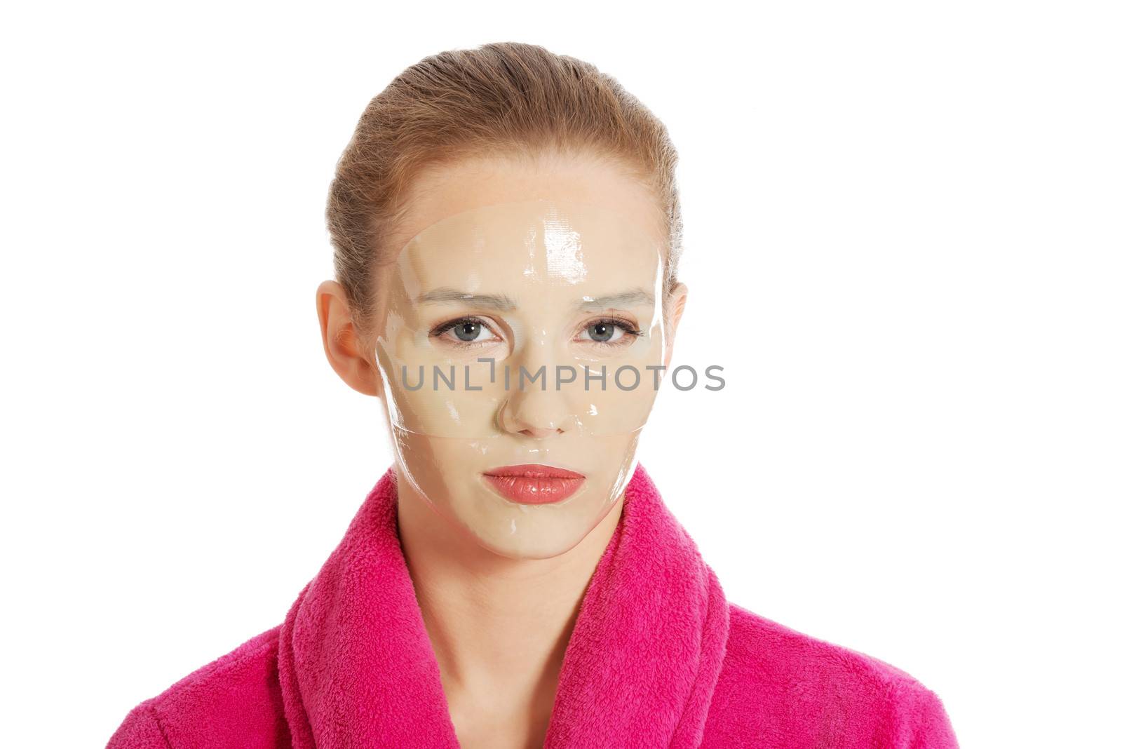 Beautiful woman in pink bathrobe and havinf facial mask. Isolated on white.