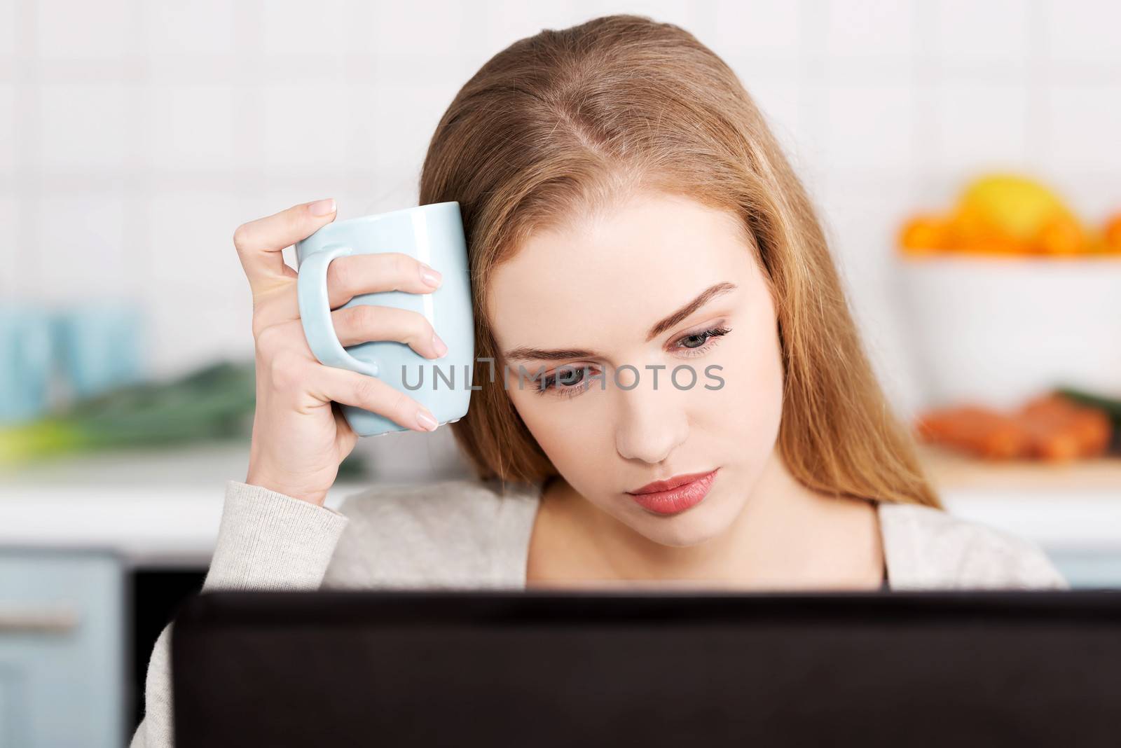 Beautiful caucasian woman sitting with hot drink and working on laptop. Indoor background.